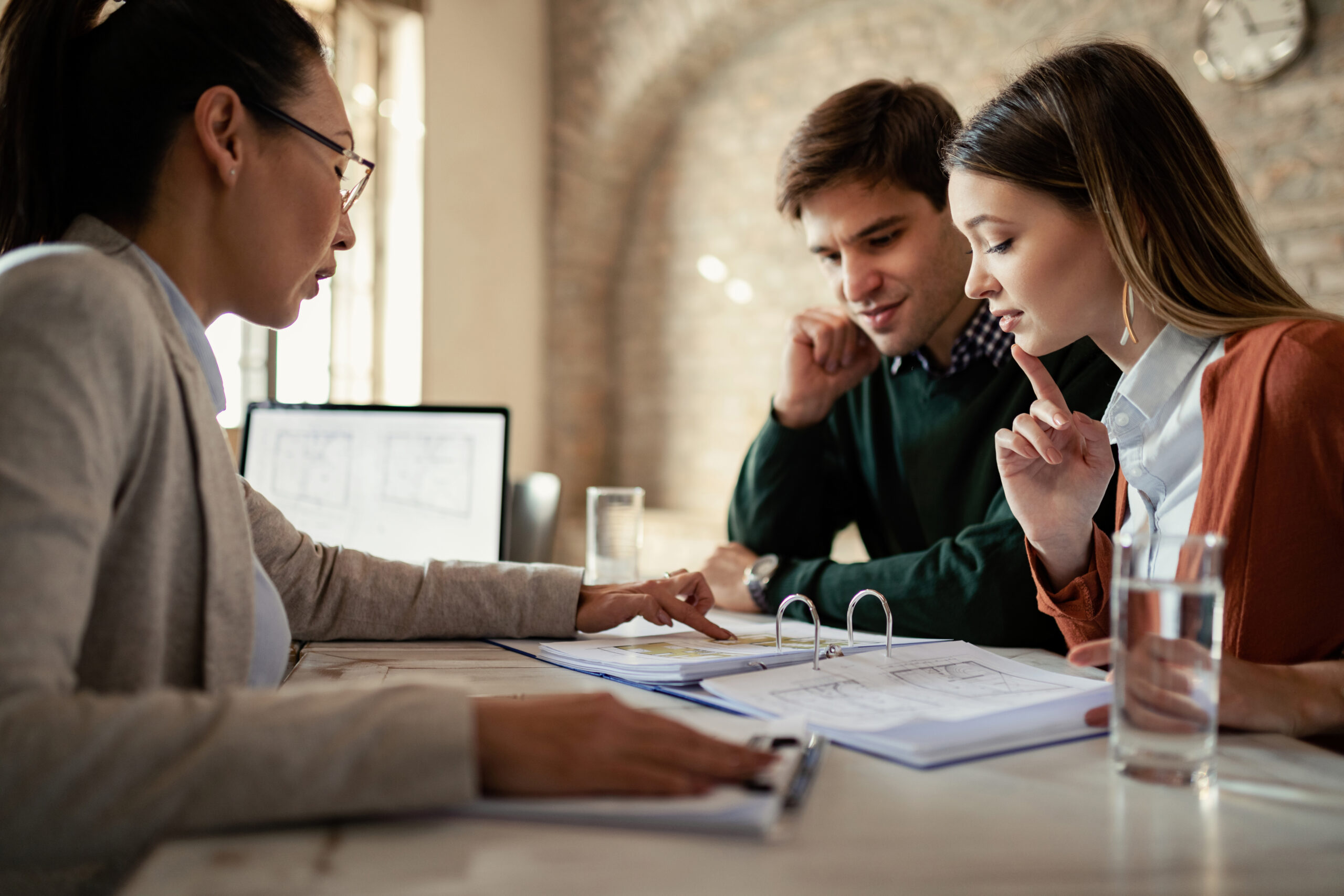 young man his wife examining housing plans with real estate agent meeting office scaled